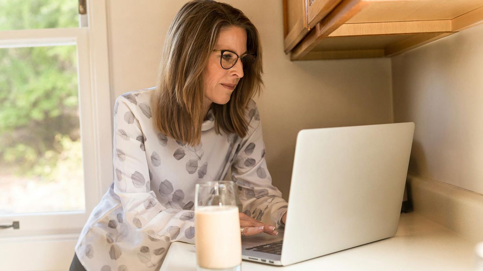 Woman using her computer in the kitchen counter drinking a glass of milk